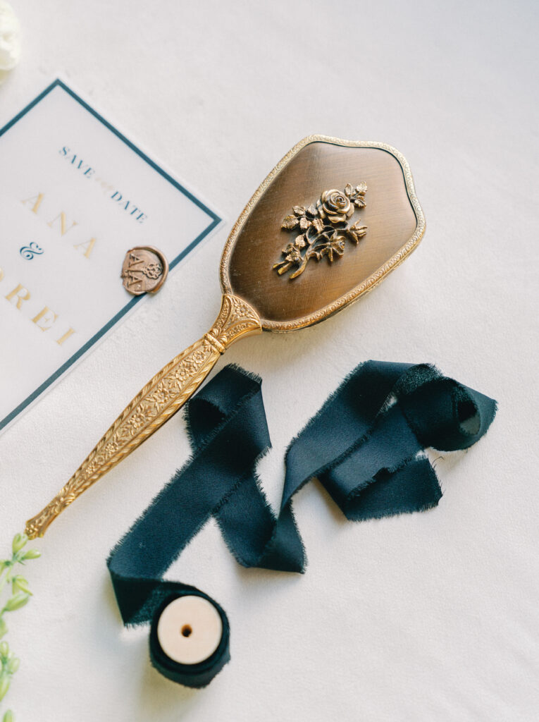 Luxury wedding invitation suite with vintage gold hand mirror, custom wax seal, and elegant dark green silk ribbon flatlay