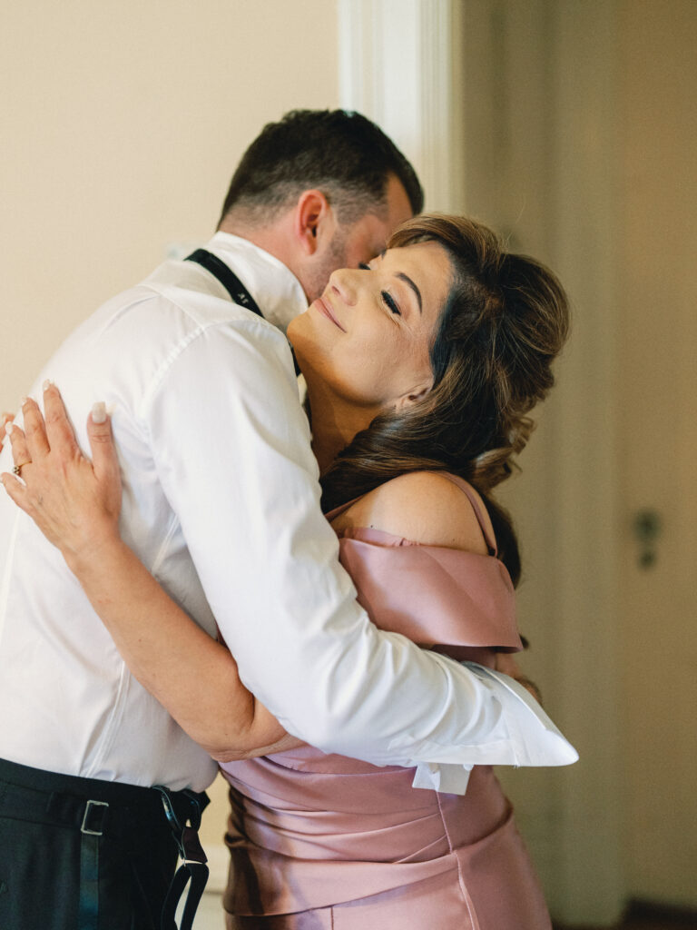 Candid wedding day photoshoot featuring a heartfelt embrace between the groom and his mother.