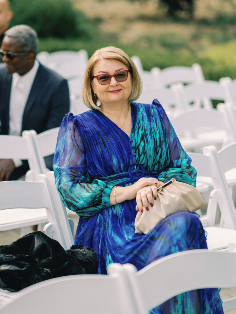Wedding guest photoshoot featuring an elegant woman in a blue dress waiting for the outdoor ceremony to begin.