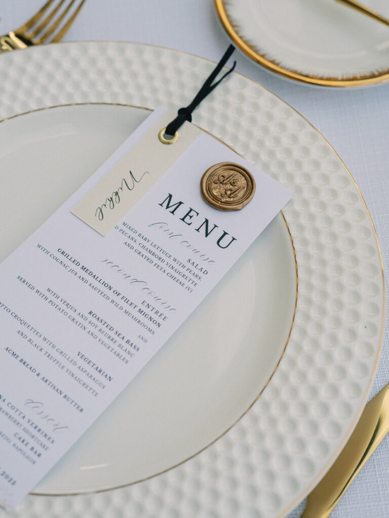 Elegant wedding menu photoshoot featuring personalized stationery with a gold wax seal on a textured dinner plate.