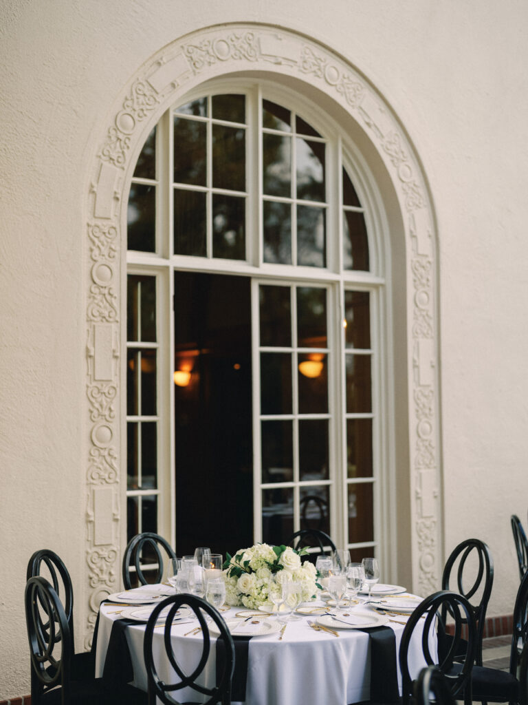 An elegant wedding reception setup on an outdoor terrace, highlighting the seamless transition from daylight to sunset through grand estate windows