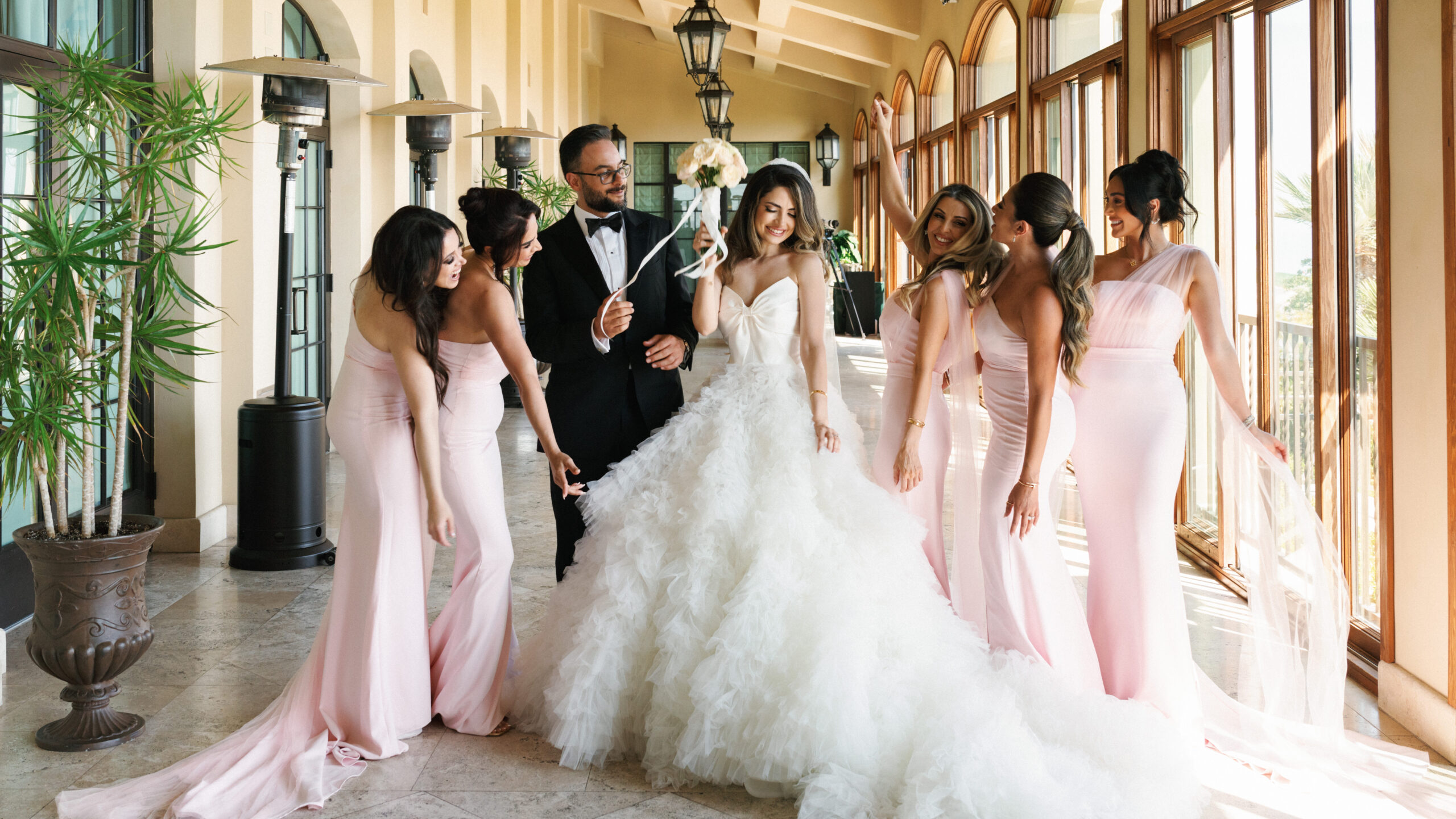 Formal wedding portraits of a bride, groom, and bridesmaids in a spacious venue terrace with abundant natural daylight