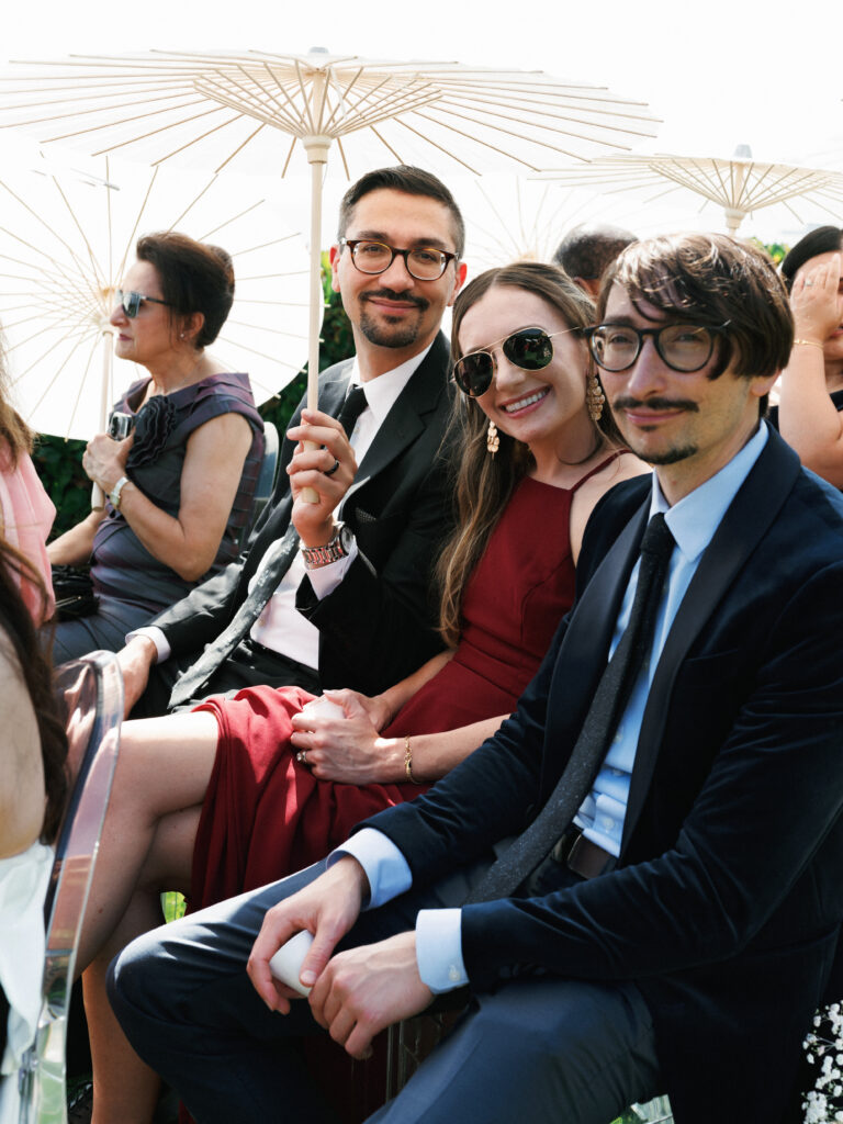 Documentary wedding photography capturing stylish guests during an outdoor cocktail reception with clear chairs and sun protection