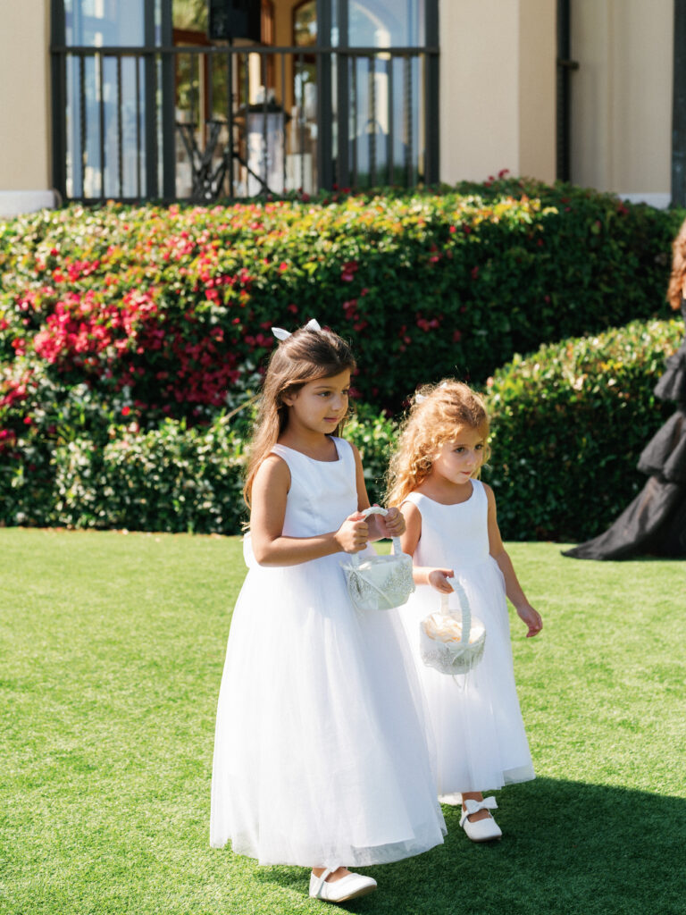 Outdoor destination wedding ceremony layout featuring flower girls during the processional on a vibrant green lawn