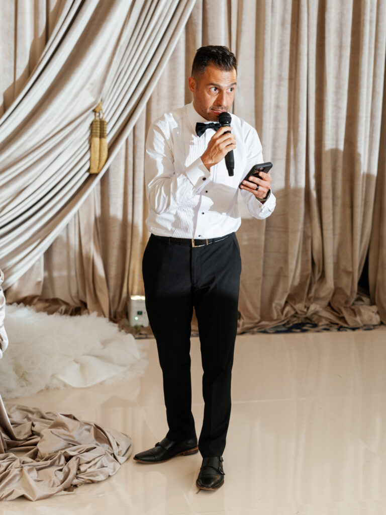 Best man in a white dress shirt and bow tie delivering a toast during the wedding reception.