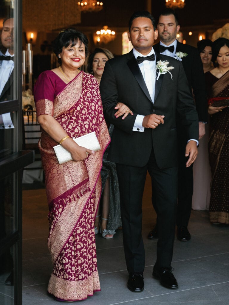 Groom walking down the aisle with his mother wearing a traditional Indian saree during the wedding processional