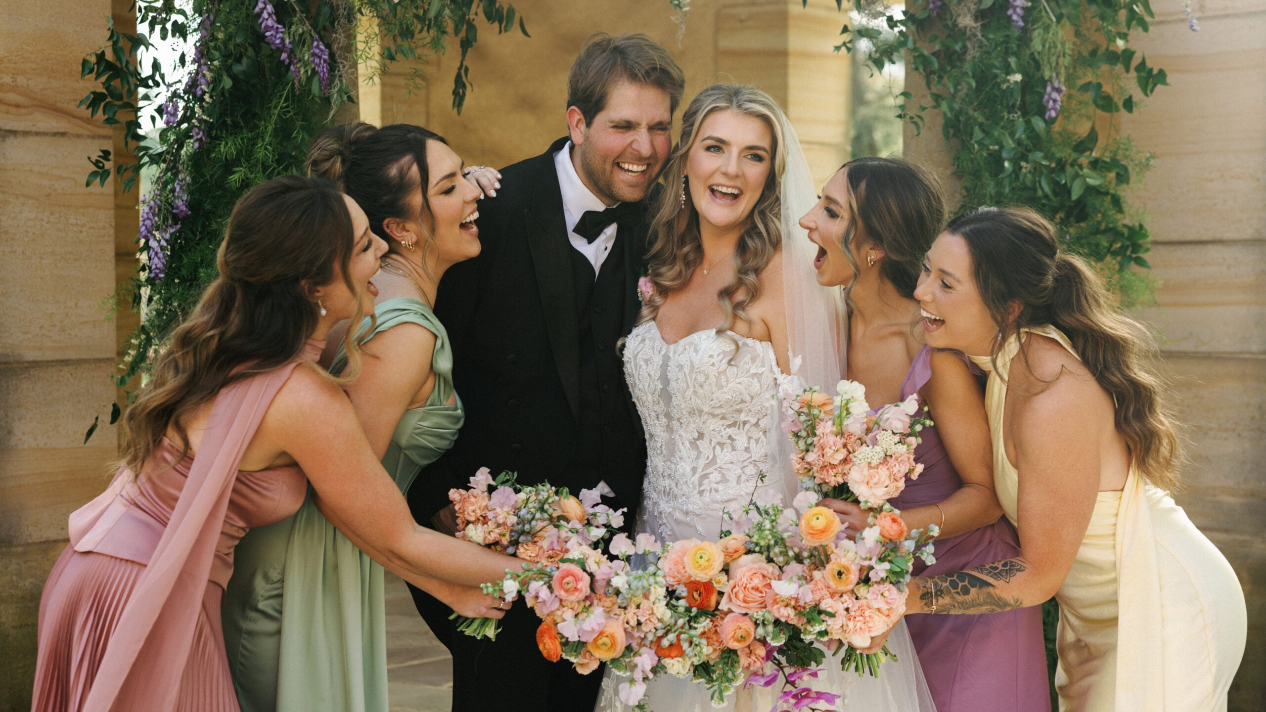 Bride and groom sharing a joyful moment with friends under a floral arch at a luxury villa wedding