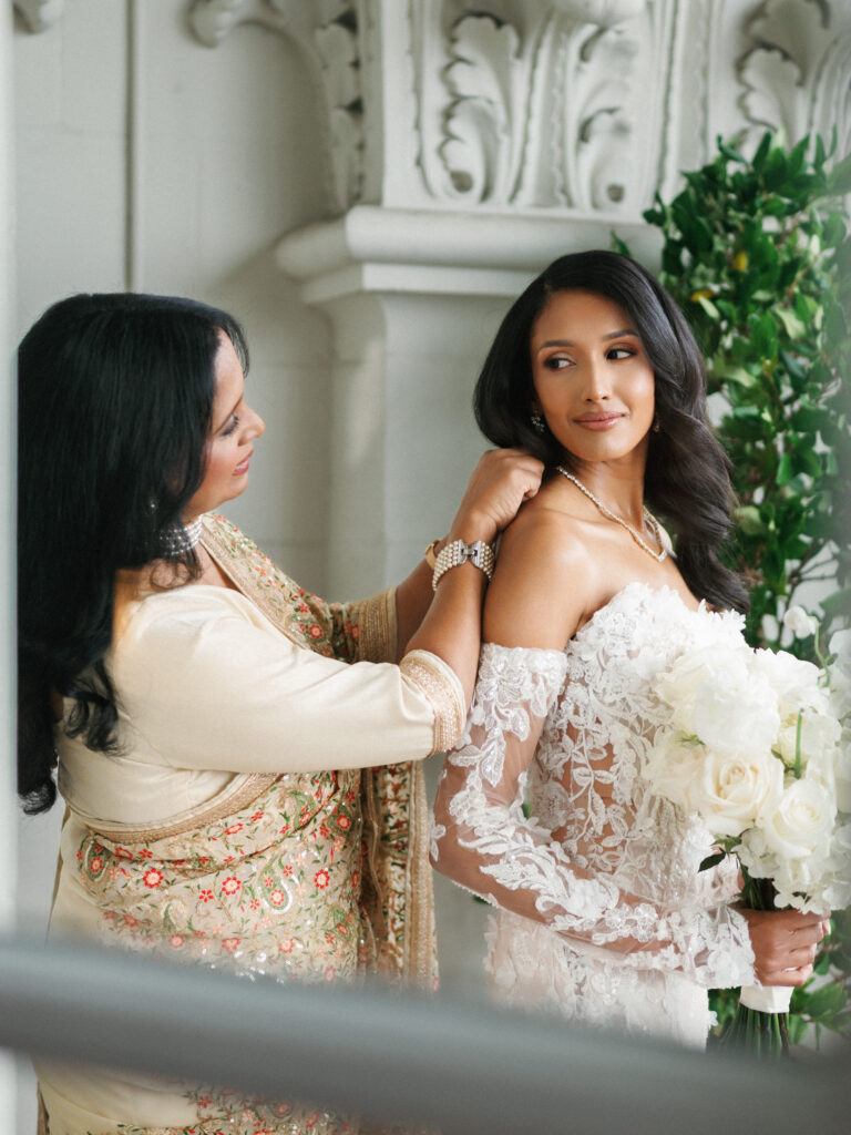Touching wedding day moment as a mother in traditional saree helps the bride with her dress.