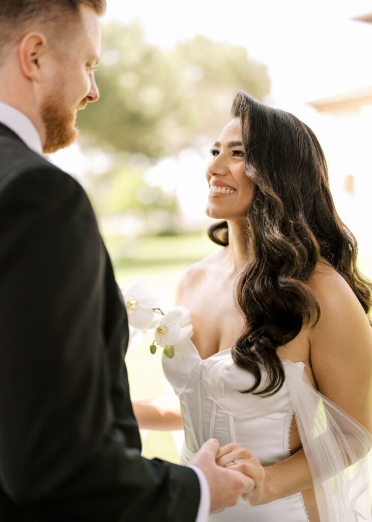 Candid wedding couple photoshoot with a happy bride smiling warmly at her groom outdoors.