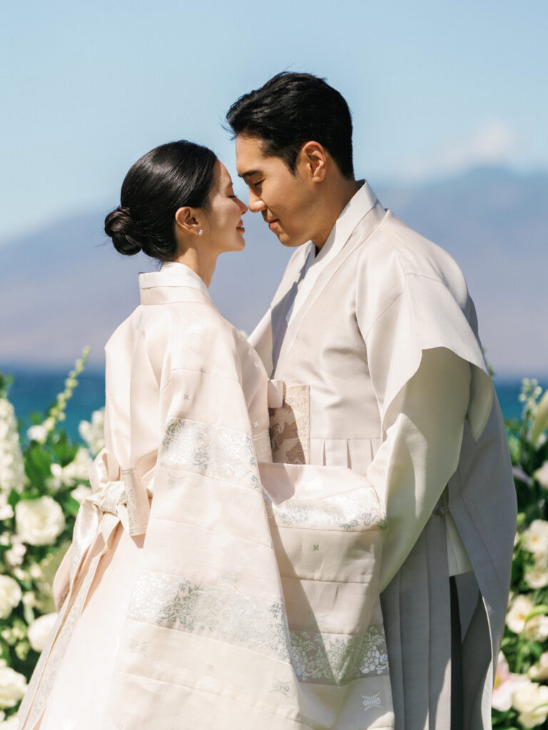 Bride and groom in elegant silk Korean traditional Hanbok attire sharing an intimate moment at a luxury outdoor wedding by the ocean