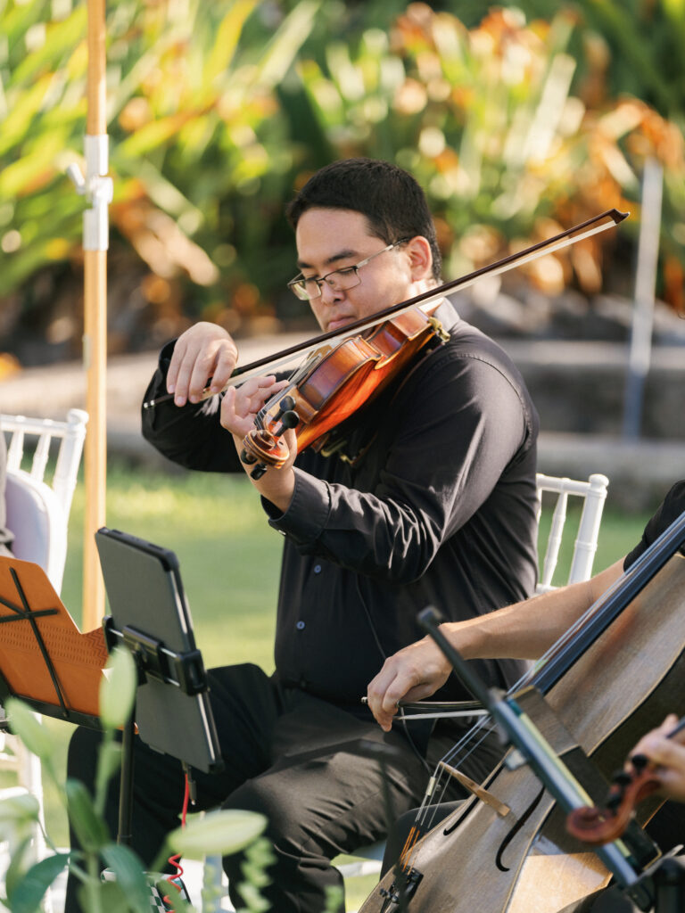 A professional violinist playing live music during an outdoor luxury wedding ceremony with a cello player nearby