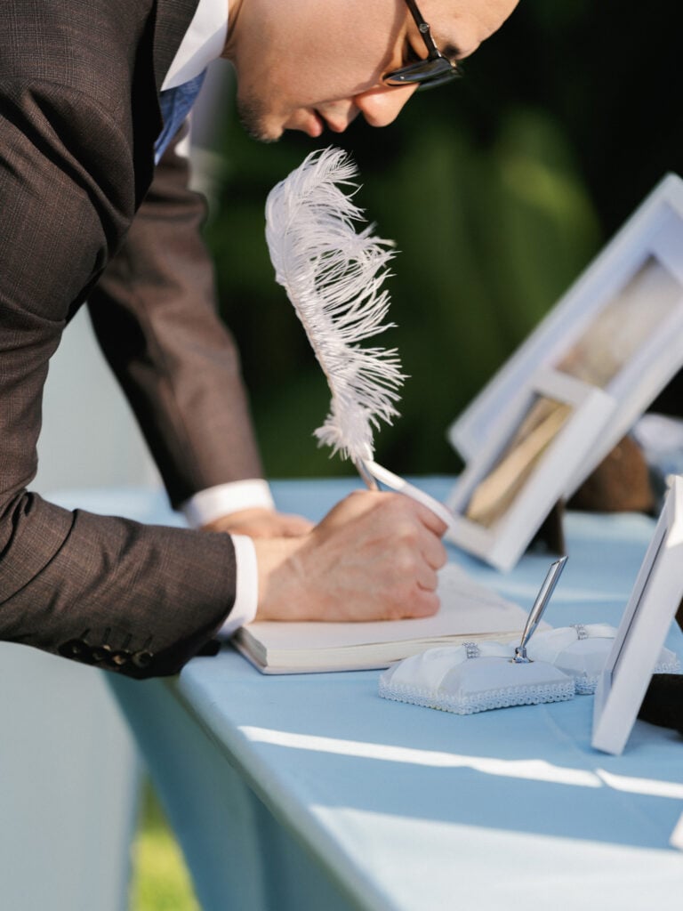 Elegant wedding signing table with a guest book, white quill pen, and silver pen holders on a pastel blue tablecloth