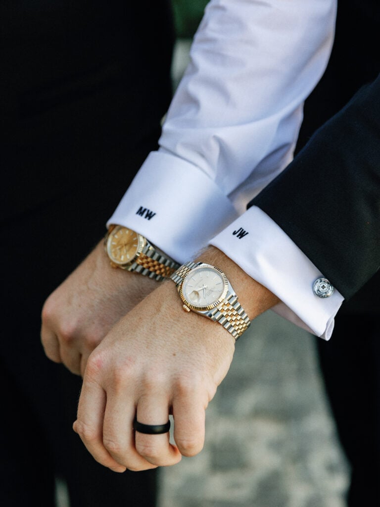 Close up of a groom and best man wearing luxury watches and white dress shirts with custom embroidered initials on the cuffs