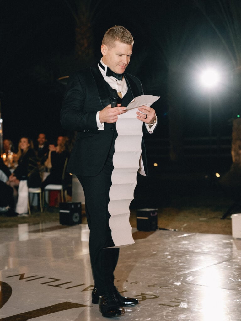 Best man or groom reading a funny long wedding speech from a long scroll of paper during the reception dinner