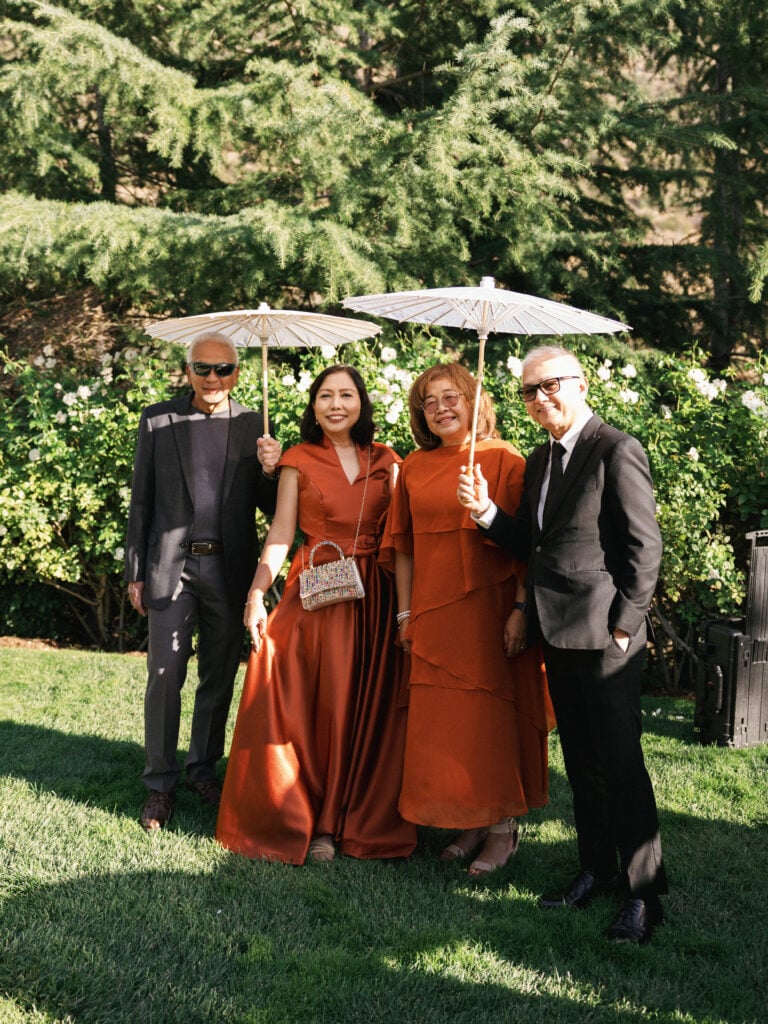 Sophisticated guests in formal attire and rust-colored satin dresses posing with sun parasols at an upscale estate wedding reception