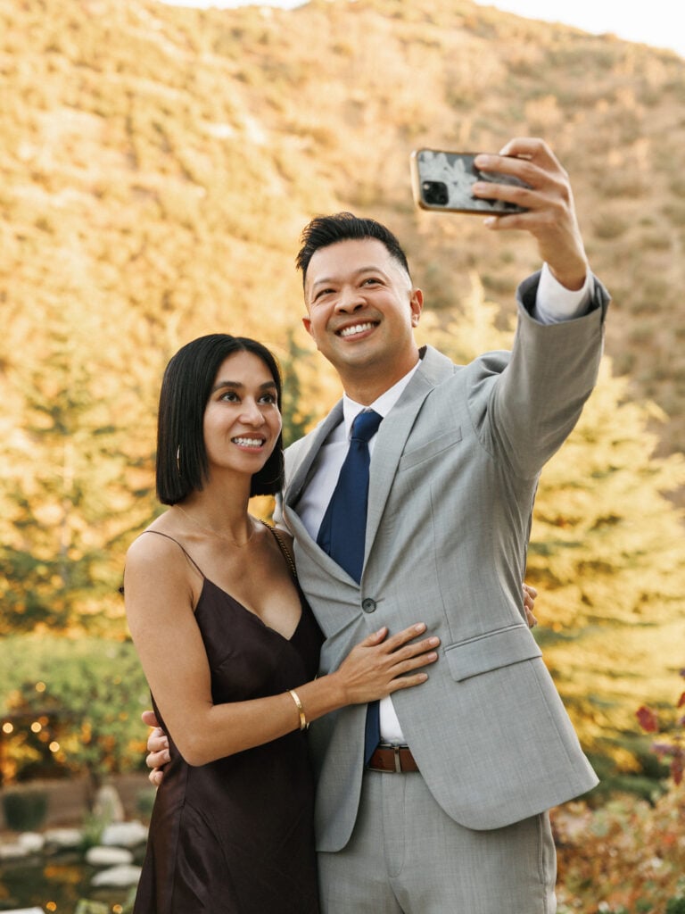 Smiling wedding guests taking a selfie on a smartphone at an outdoor luxury estate reception