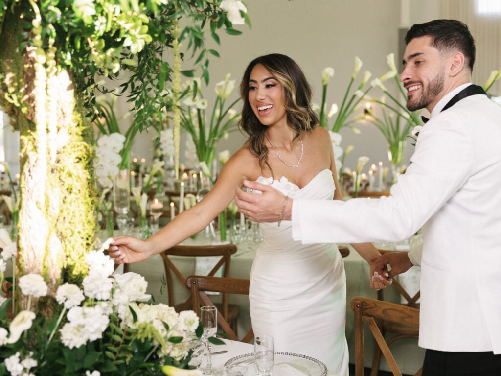 Smiling bride in a strapless dress and groom in a white jacket walking through a decorated wedding venue