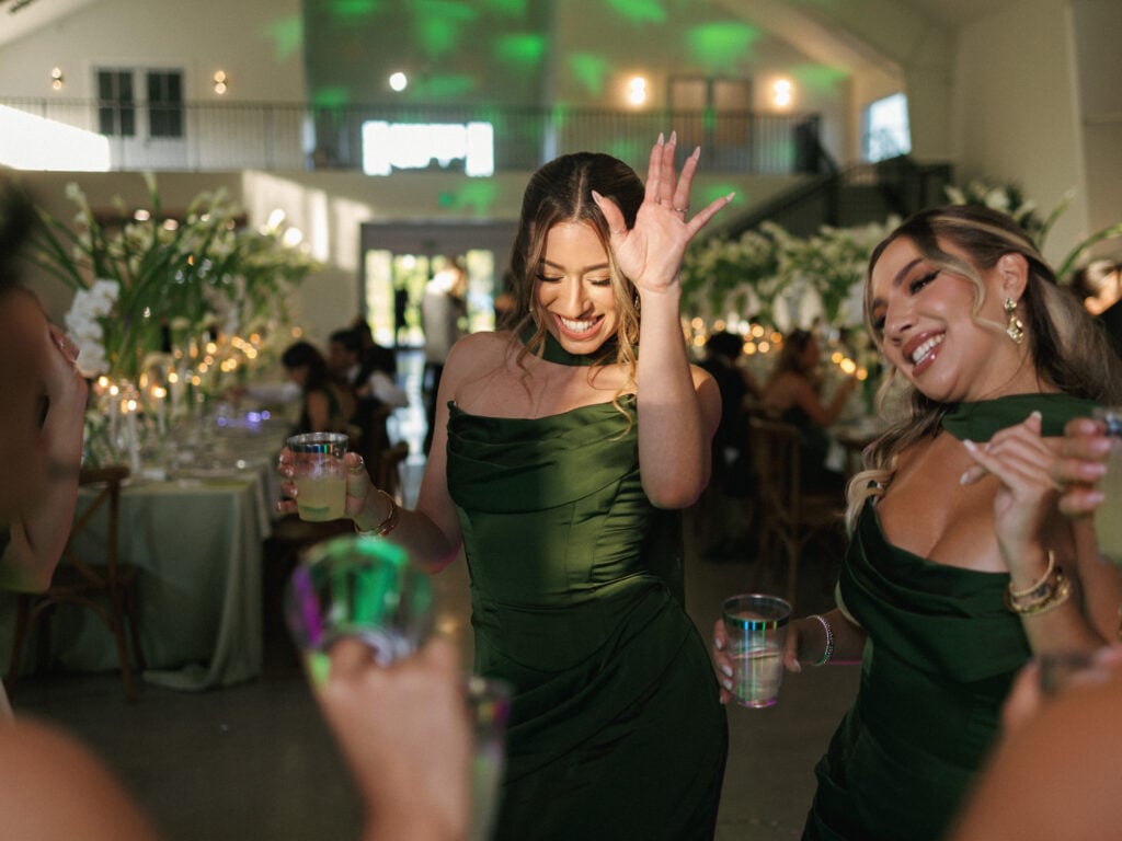 Bridesmaids in dark green dresses dancing and celebrating at a wedding reception
