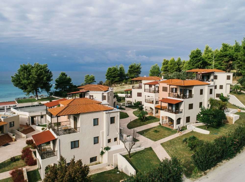 Premium coastal wedding resort architecture at Philoxenia Hotel Halkidiki, showing stone villas, pine trees, and an editorial destination wedding backdrop.