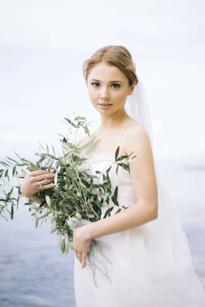 Greek chic bridal editorial featuring a bride in a strapless wedding dress holding a textured olive branch bouquet with a flowing veil