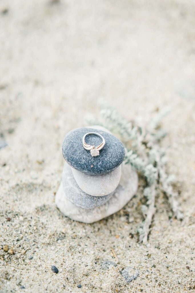Luxury diamond engagement ring styled on a stack of smooth beach pebbles and sand for a Mediterranean beach wedding.
