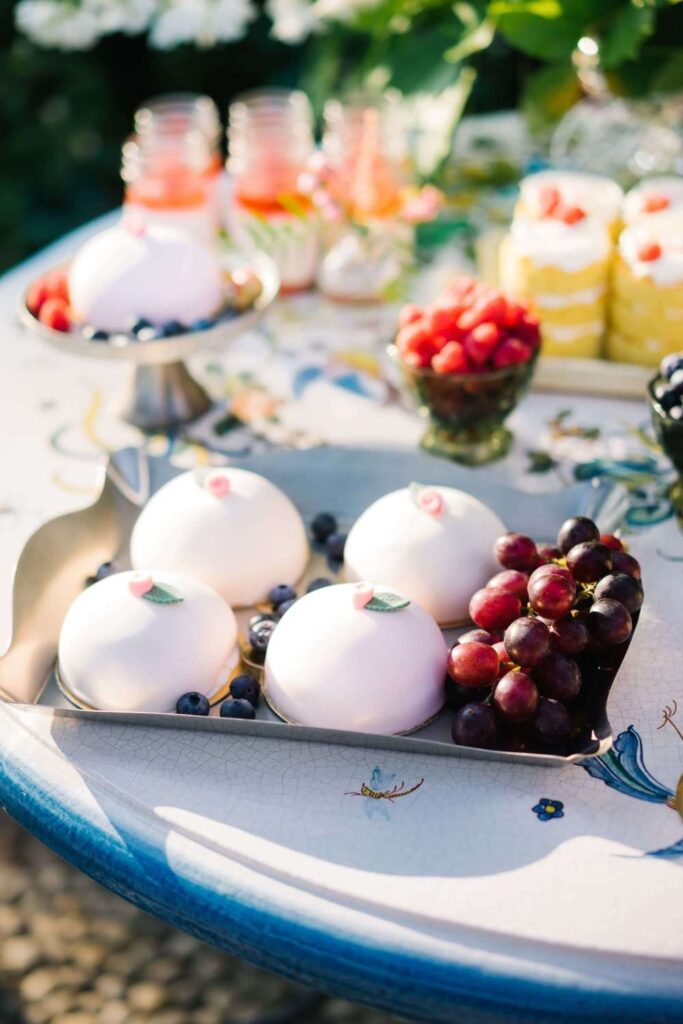 Luxury wedding dessert bar featuring elegant dome mousse cakes, fresh grapes, and mini wedding cakes styled on a Mediterranean mosaic table