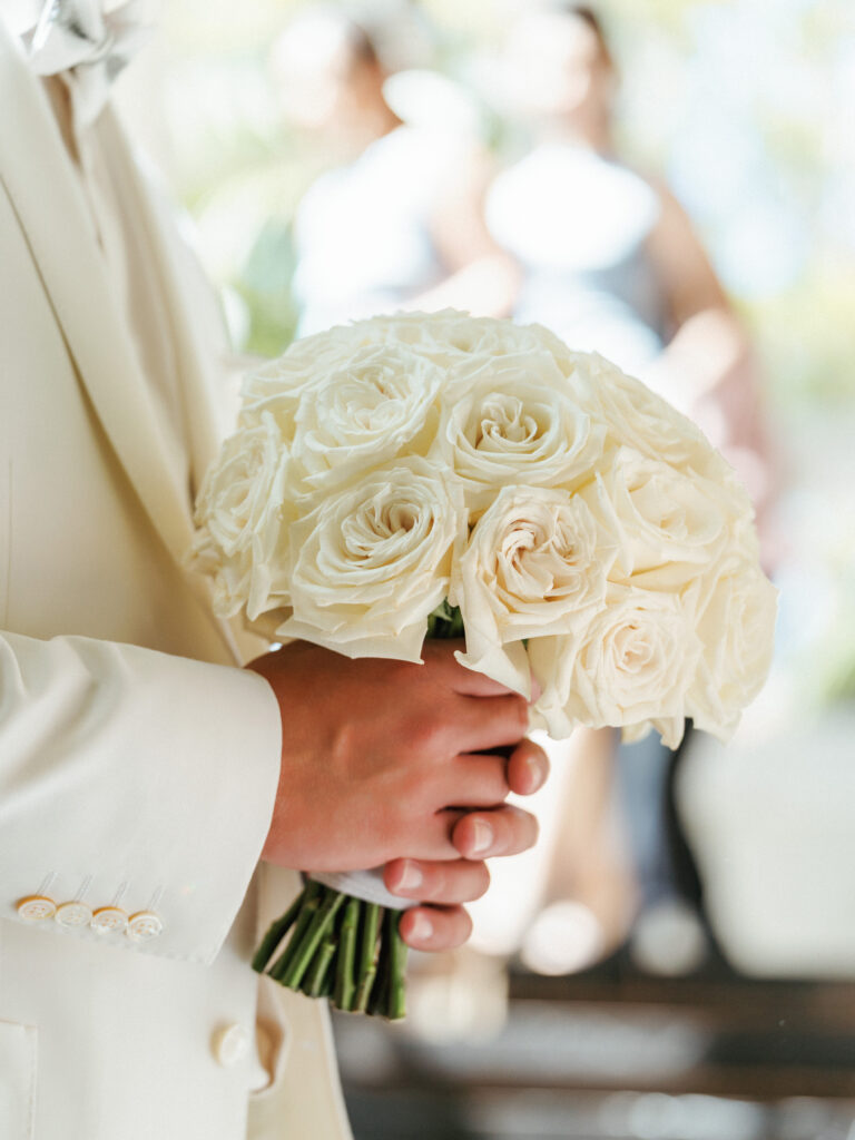Professional wedding details photography of a round bridal bouquet with white roses during a couple's photoshoot.
