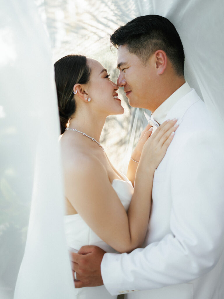 Romantic wedding couple photoshoot featuring a bride and groom embracing under a flowing white veil.