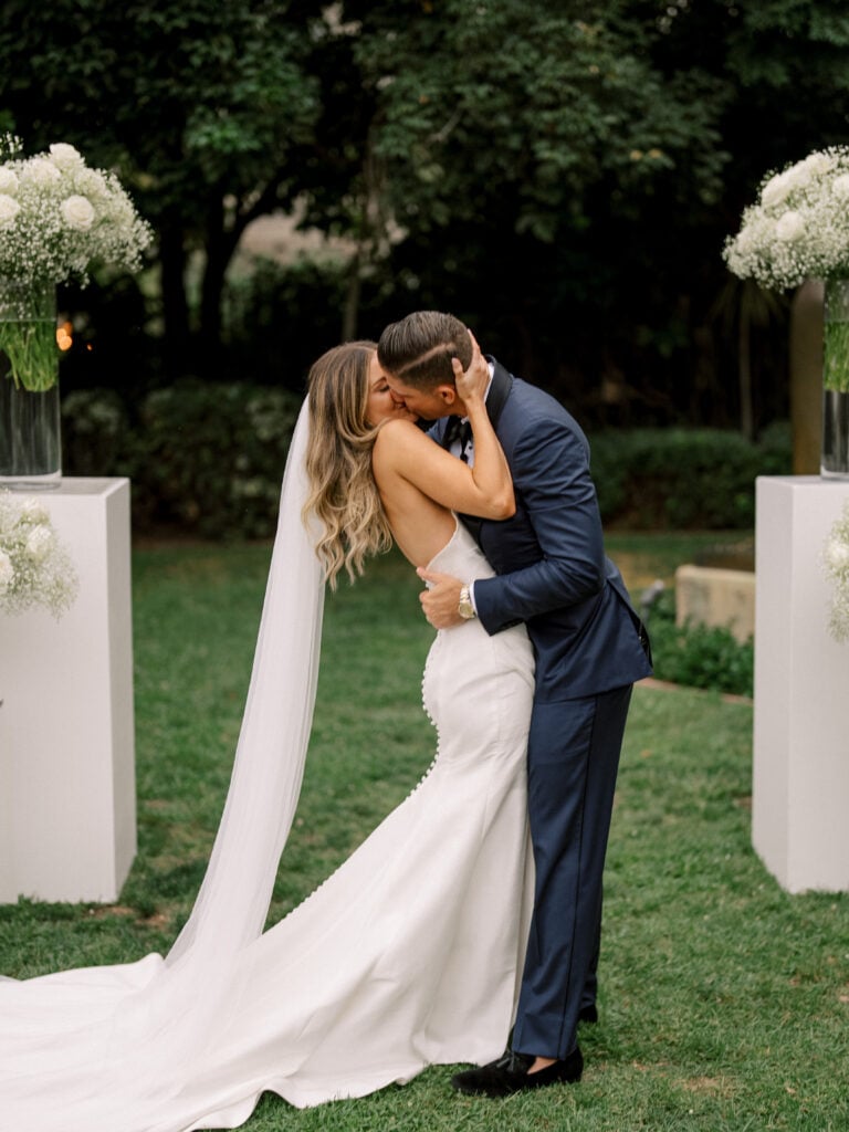 Bride and groom sharing a romantic first kiss at the altar during an outdoor wedding ceremony