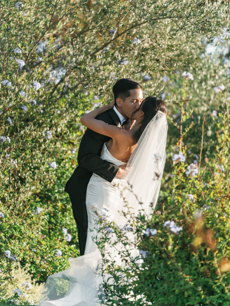Intimate wedding first look moment with a bride and groom kissing in a lush garden.