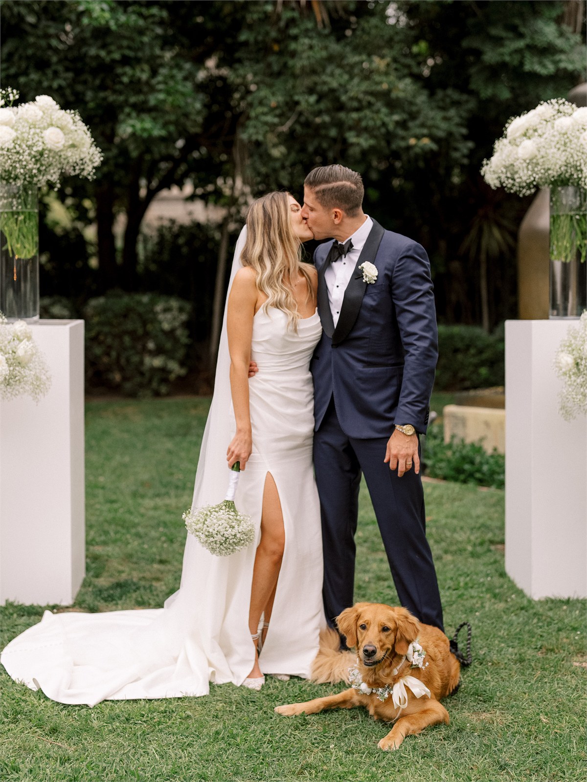 Wedding couple standing with a dog beneath floral arches