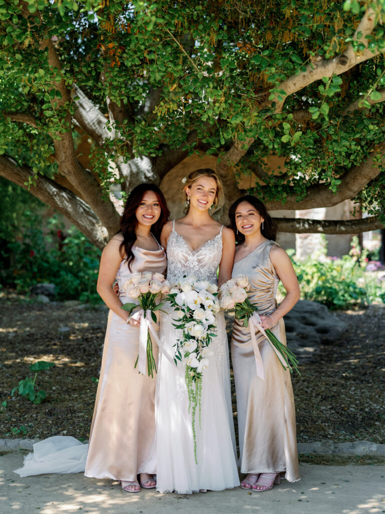High-end bridesmaid inspiration featuring a modern bride with romantic pastel bouquets and bridal party in neutral silk dresses on a sunlit estate lawn.