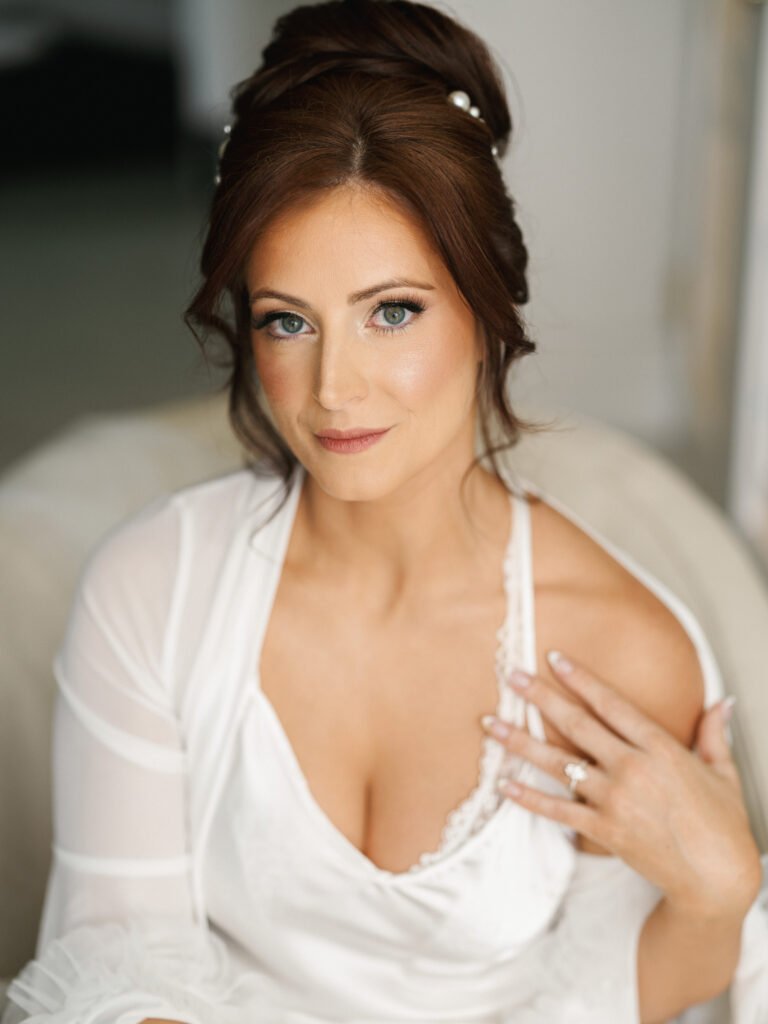 A close-up bridal portrait highlighting elegant wedding updo hair and professional glam makeup during morning preparation.