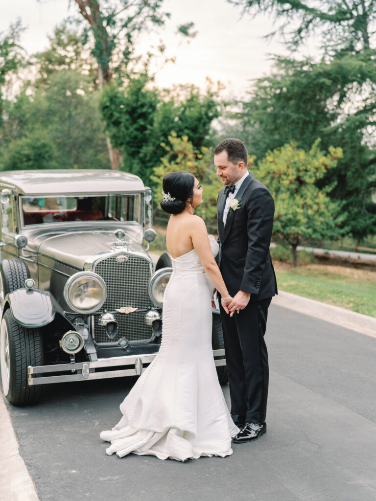 Elegant Los Angeles wedding photography featuring a newlywed couple in black-tie attire posing with a classic antique car.