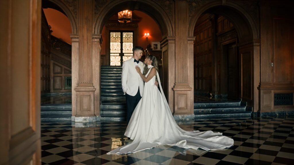 Bride and groom standing embraced in the Great Hall at Greystone Mansion, showcasing the historic black and white checkered marble floor and carved wood arches during a photo session.