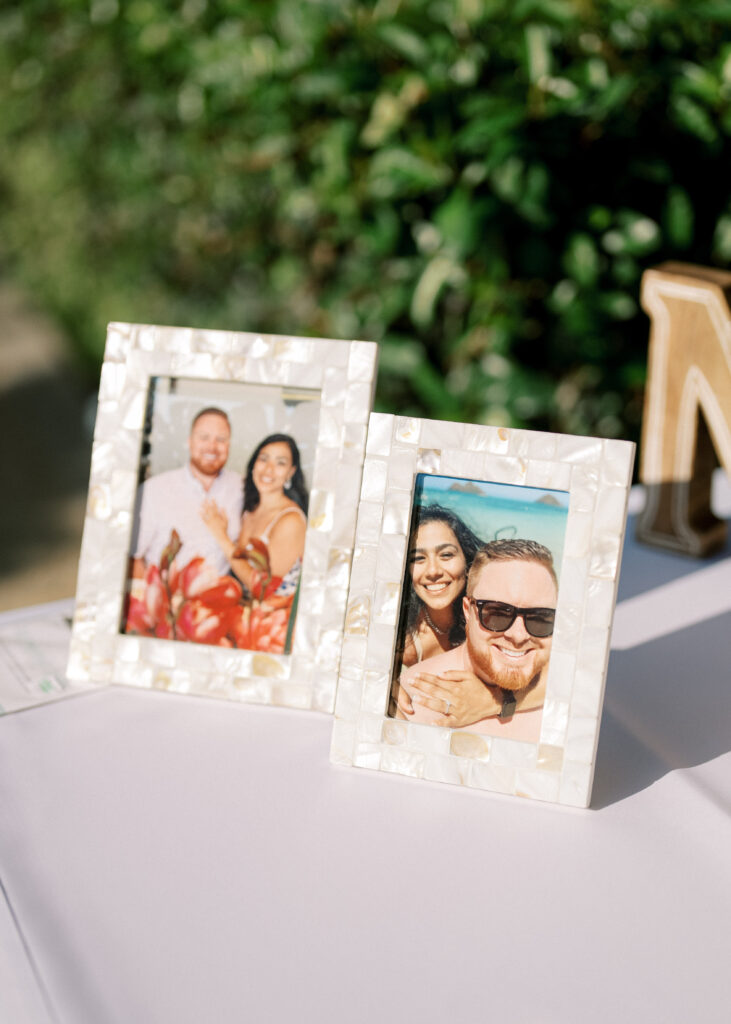 Mother of pearl mosaic photo frames displaying couple pictures on a welcome table, captured for timeless wedding detail photos next to green bushes.