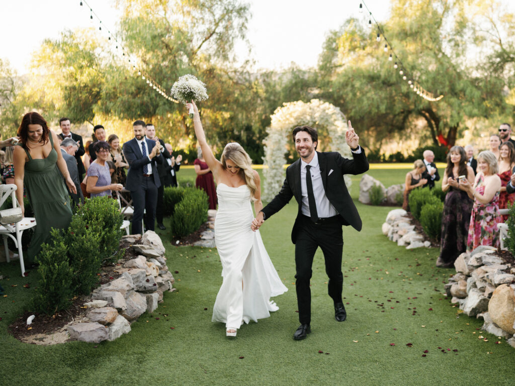 Dynamic wedding videography still capturing newlyweds running down the aisle while guests applaud at a luxury garden venue.