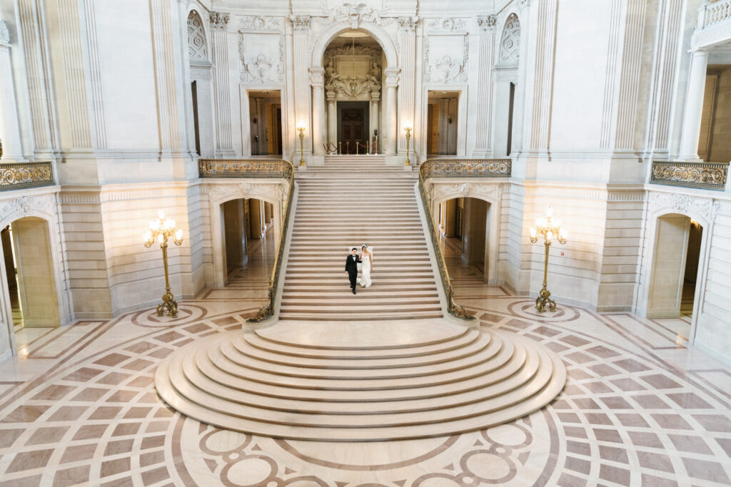 Bride and groom walking down the grand staircase inside the historic San Francisco City Hall.