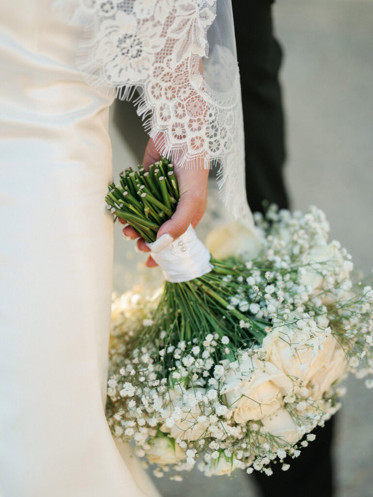 Bride holding a modern all-white wedding bouquet wrapped in satin ribbon with elegant pearl pins.