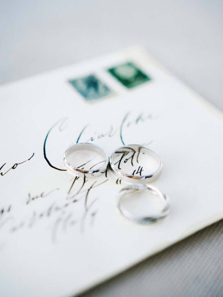 Platinum wedding bands and a diamond eternity ring resting on an elegant fine art calligraphy letter with vintage stamps for timeless wedding detail photos.