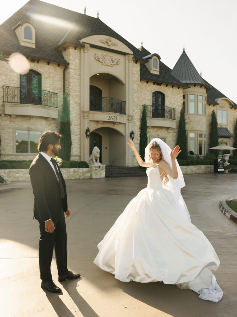 Joyful bride twirling in a ballgown at a multicultural wedding celebration outside a luxury venue.