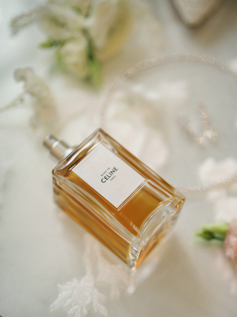 Celine luxury perfume bottle arranged on a bright white flat lay layout with delicate white flowers, silk ribbons, and a crystal necklace.