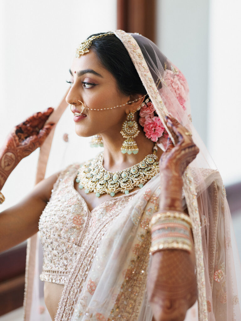 Bridal portrait of a South Asian bride wearing traditional jewelry and a dupatta veil at a multicultural wedding.