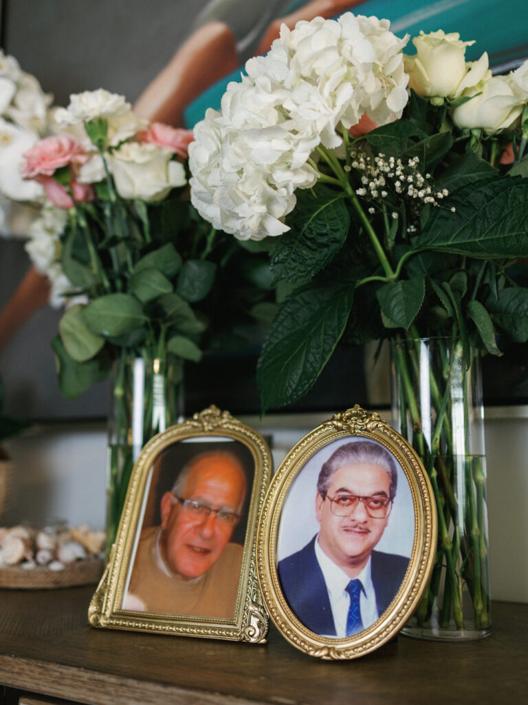 Vintage gold oval photo frames honoring deceased family members on a wedding memory table next to glass vases with white hydrangeas and roses.