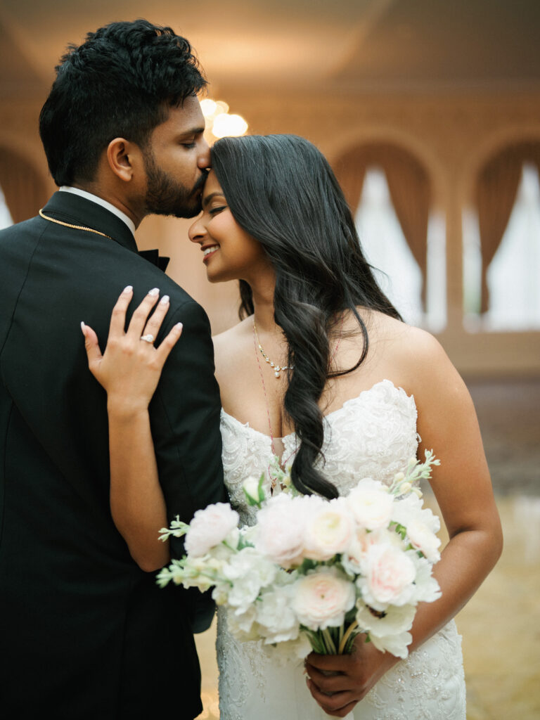 A groom kisses his bride's forehead during an intimate portrait session at a luxury New York City ballroom wedding.
