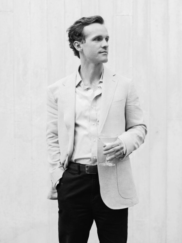Black and white editorial portrait of a modern groom looking away against a minimalist textured background.