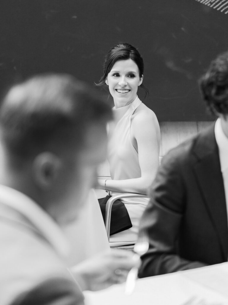 Cinematic black and white still capturing an intimate, unscripted glance from the bride during an upscale rehearsal dinner.