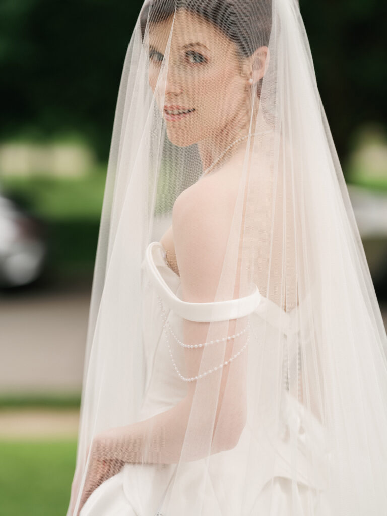 Close-up wedding photography shot of a bride looking over her shoulder through a sheer tulle cathedral veil.
