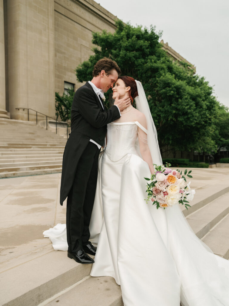Candid videography moment as the groom gently lifts the bride’s chin during a quiet romantic escape outside the museum.
