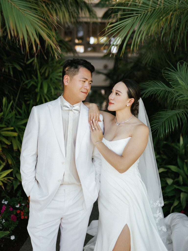 Bride and groom standing together looking at each other, with the bride leaning her arm on the groom's shoulder, wearing a white strapless dress and the groom in a white tuxedo at The Ritz-Carlton, Laguna Niguel.